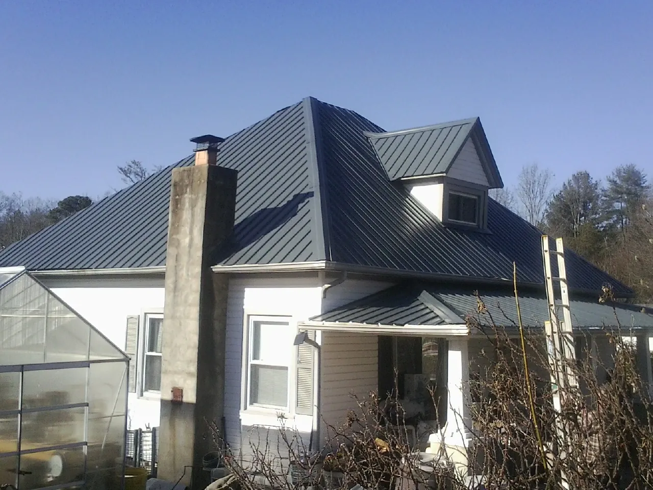 Dark blue standing seam metal roof on a white farmhouse with dormer — Slate & Tile Roof Repair by Roofing Brothers in Sun Prairie