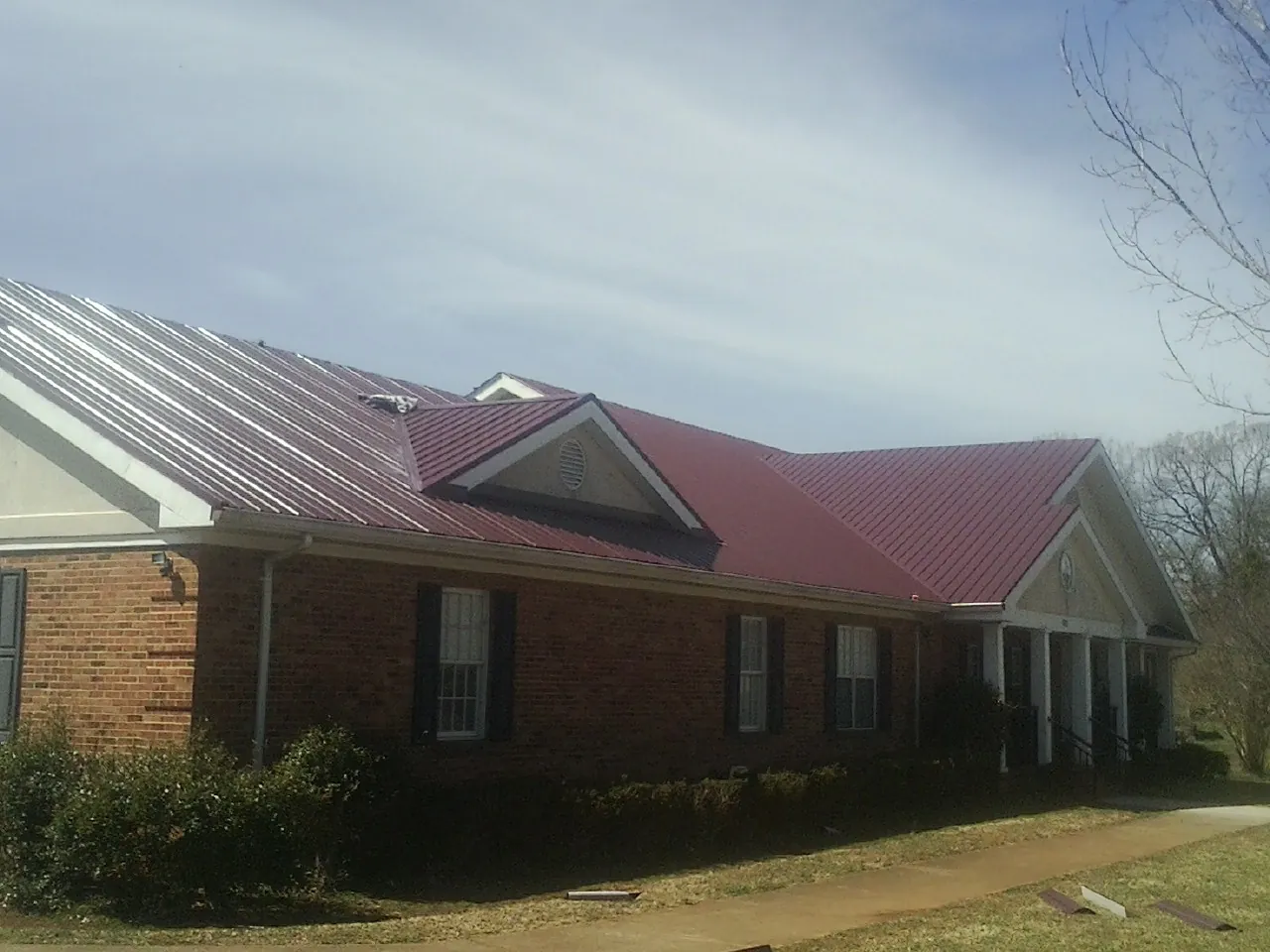 Red metal roof with gabled entries on a long brick building, from a Hail Damage Roof Repair job in Sun Prairie