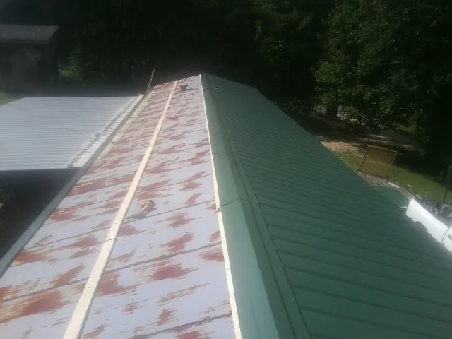 Old rusted panels beside newly installed green metal roofing — Wind Damage Roof Repair by Roofing Brothers in Sun Prairie