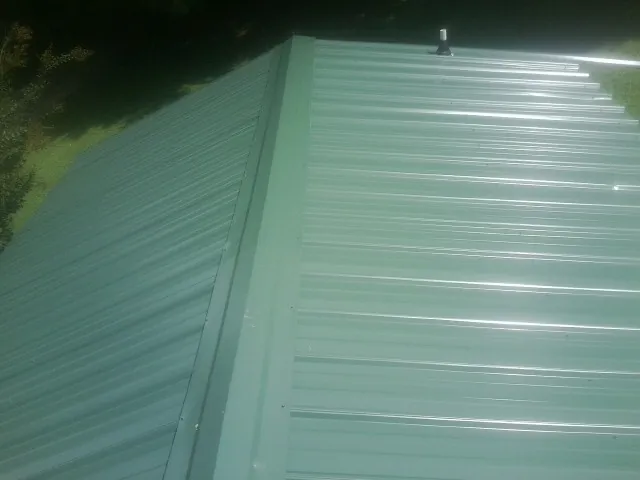 New green metal panels meeting at the ridge of a roof — Flat Roof Repair work by our crew in Sun Prairie