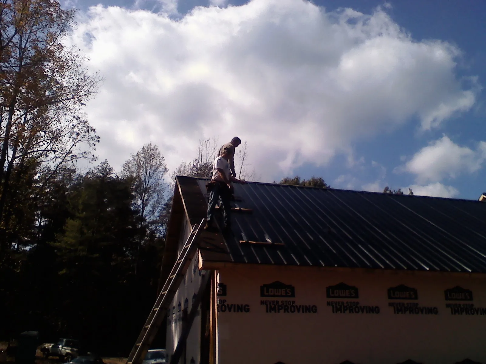 Roofer fastening dark metal panels high against a cloudy sky, from a Roof Inspection job in Sun Prairie