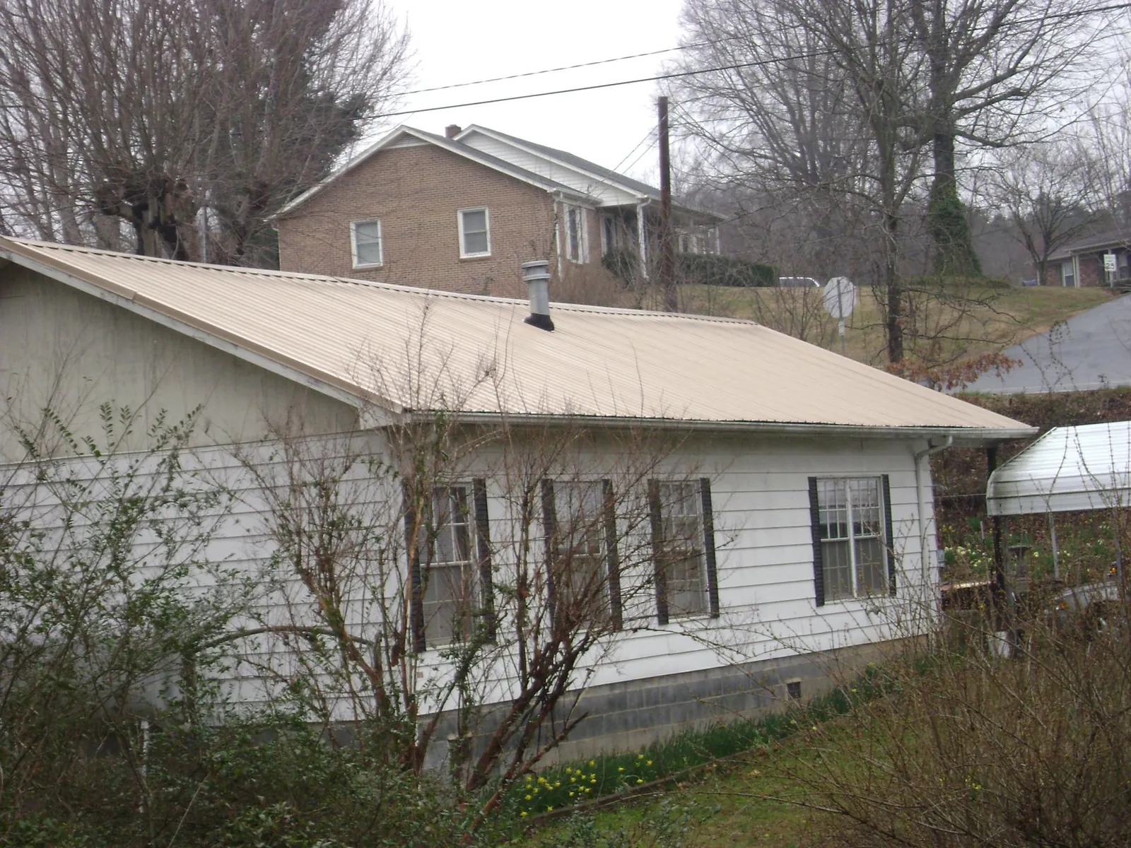 Tan metal roof on a white sided house set into a hillside — Commercial Roofing by Roofing Brothers in Sun Prairie